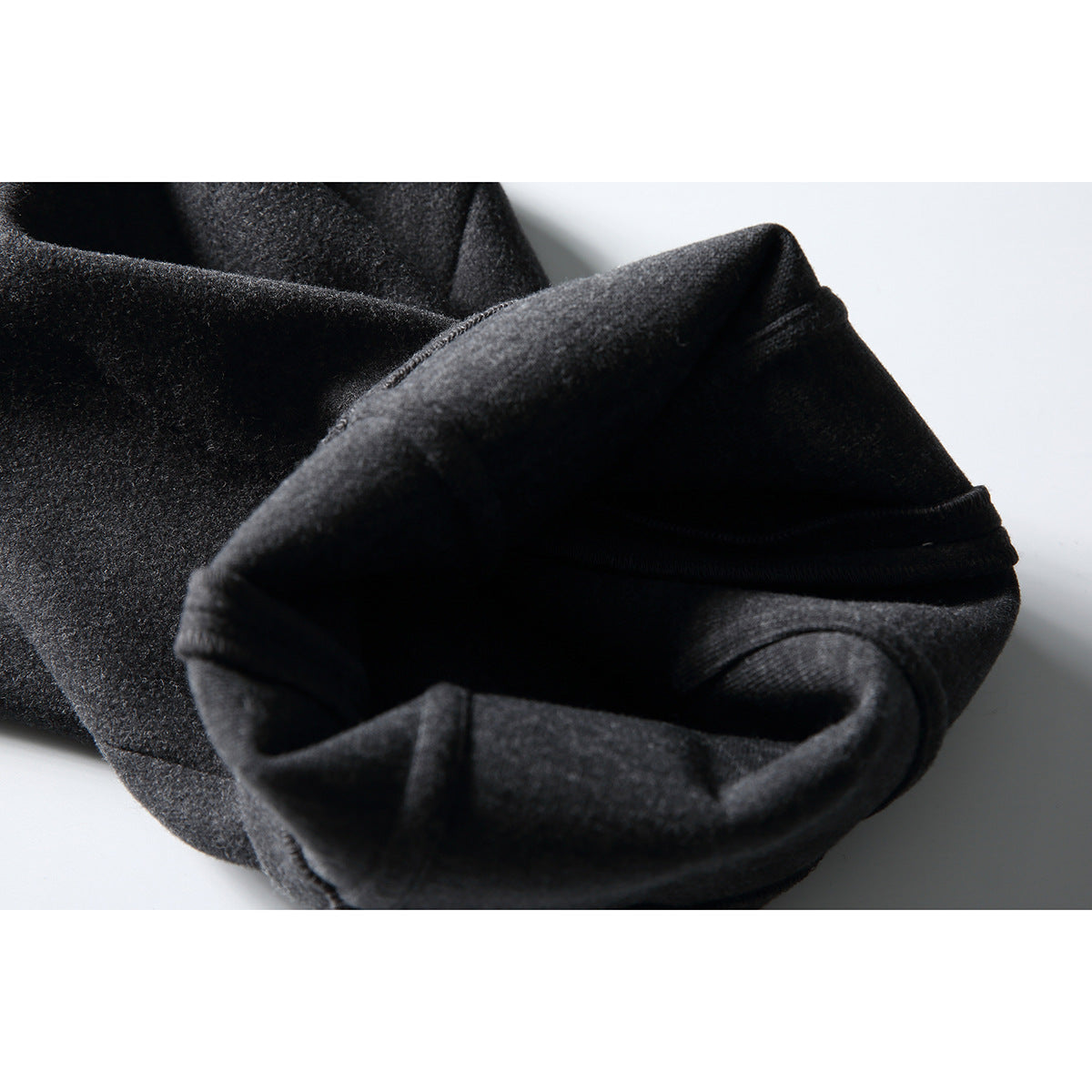 Close-up of dark charcoal trousers showing a folded fabric edge and stitched seam.