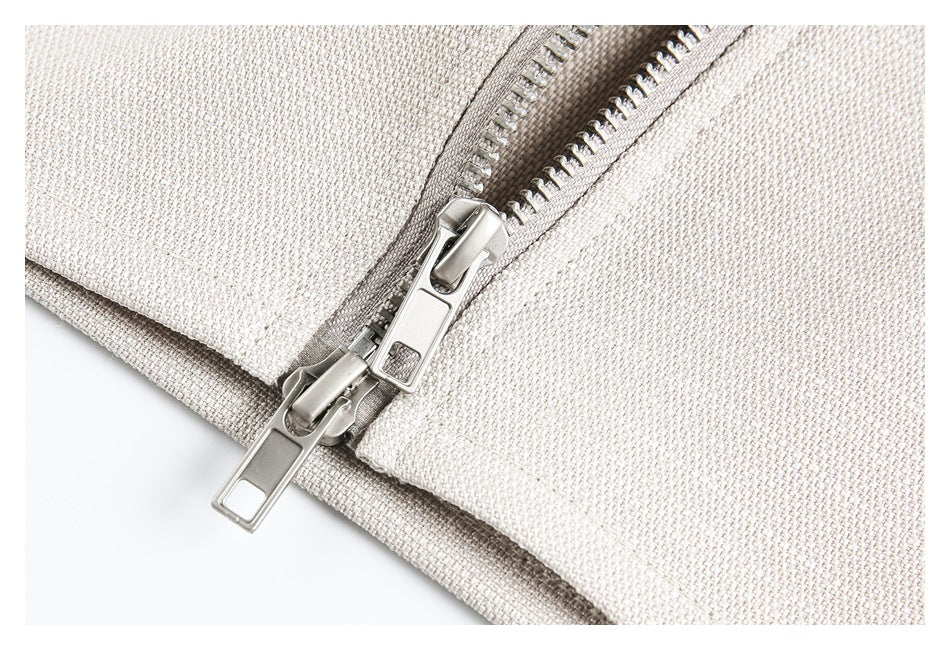 Close-up of two silver zipper sliders on ivory woven fabric.