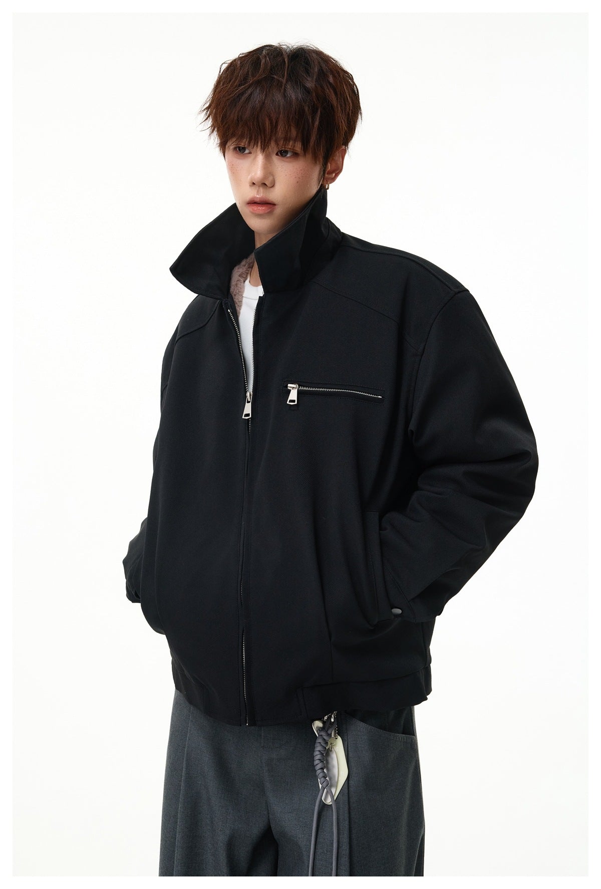 Model wearing a black zip jacket with the collar standing up, chest zip pocket and hands in pockets, over a white top