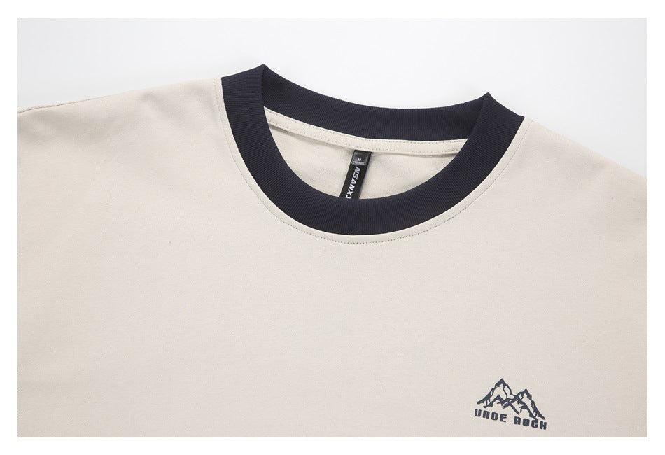 Close-up of an off-white shirt with a dark ribbed crew neck and a small mountain logo on the chest.