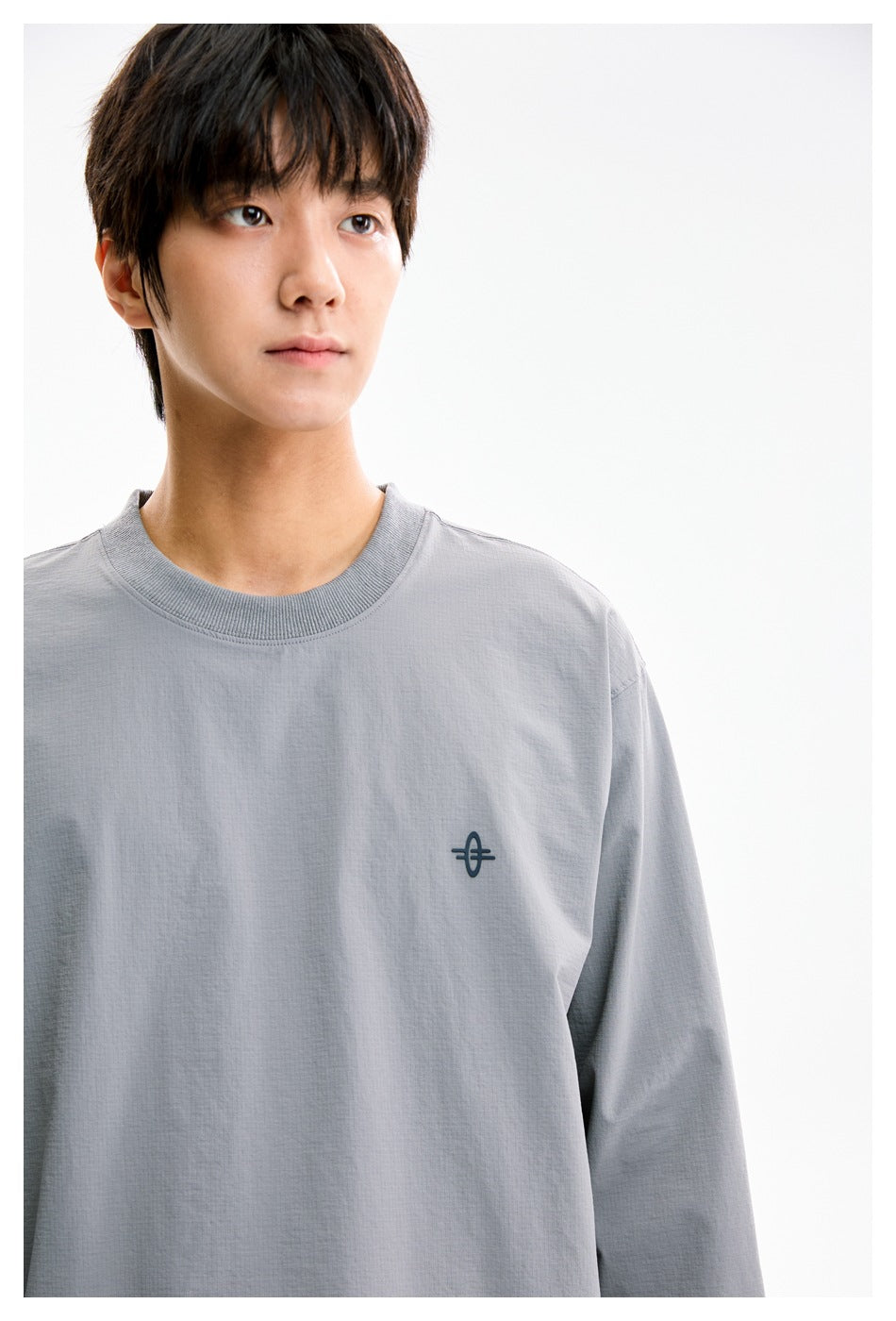 Close-up of the gray crewneck shirt on a model, showing its ribbed collar and small dark chest emblem.