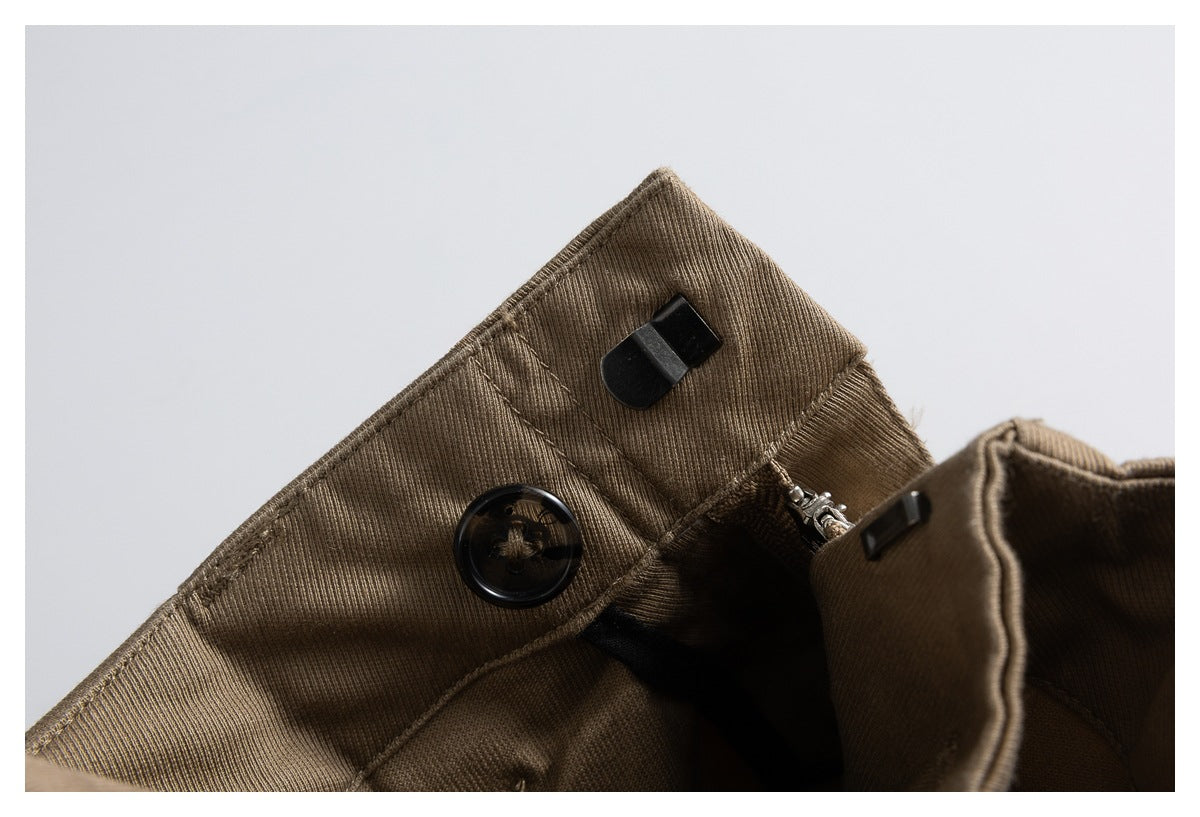 Close-up of brown trousers showing the waistband button, zipper and fly closure.