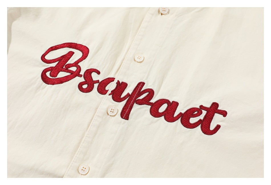 Close-up of red cursive embroidery and cream buttons on an off-white button-front garment.