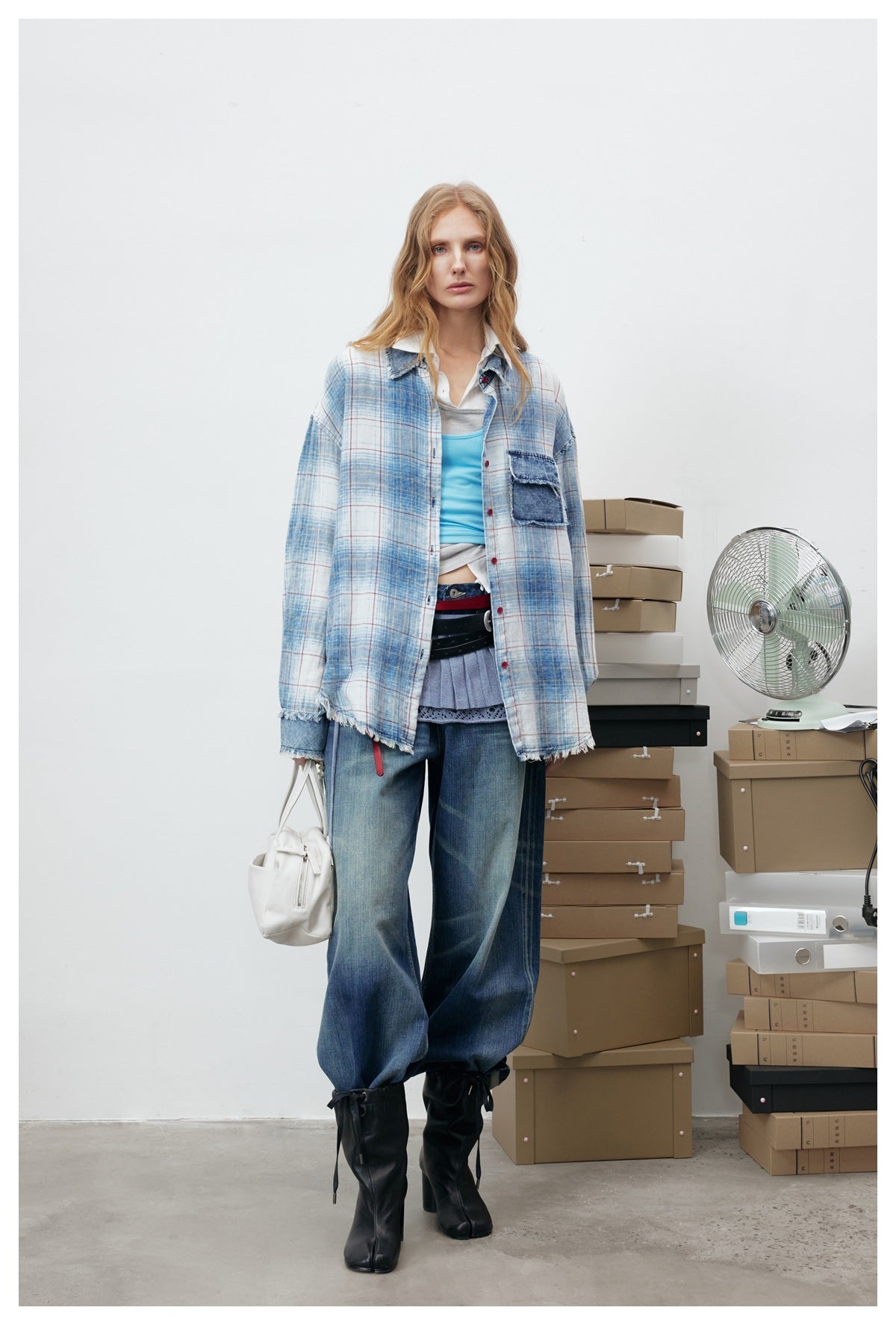 Model wearing the open plaid shirt over a blue tank top and wide-leg jeans, with white handbag and black boots