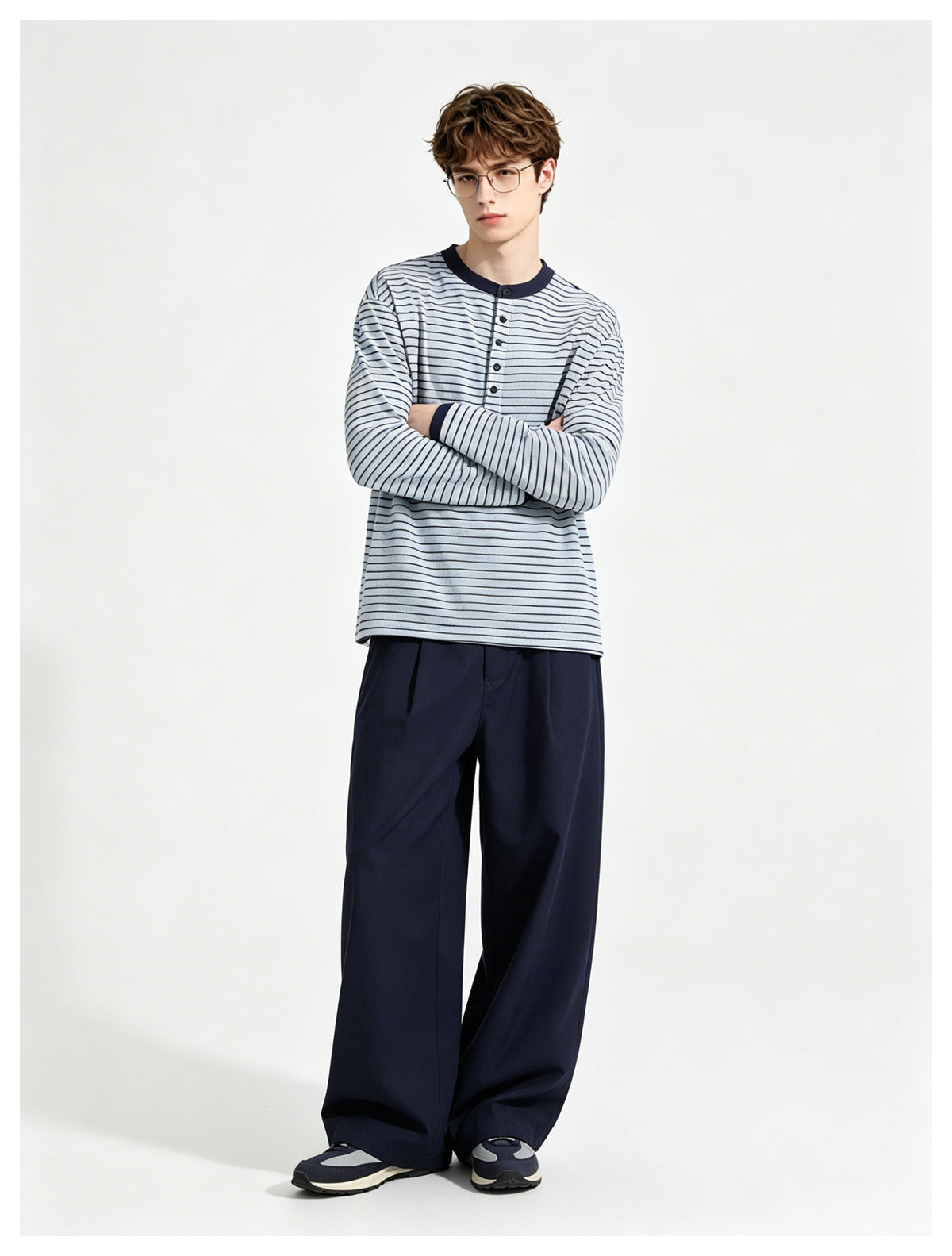 Model wearing a pale blue and navy striped long-sleeve henley with wide navy trousers, arms crossed.