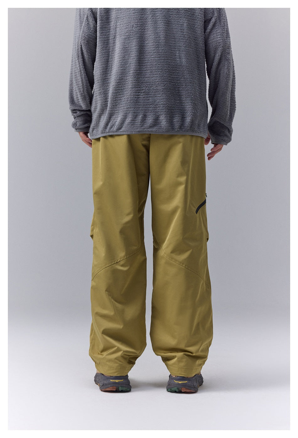 Front view of a model wearing loose olive-yellow pants with curved knee seams and gathered cuffs.