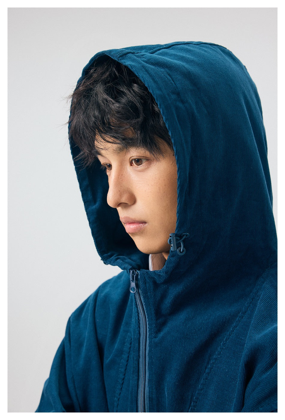 Close-up of a model wearing the deep teal hood up, showing the drawcord toggles and front zipper.