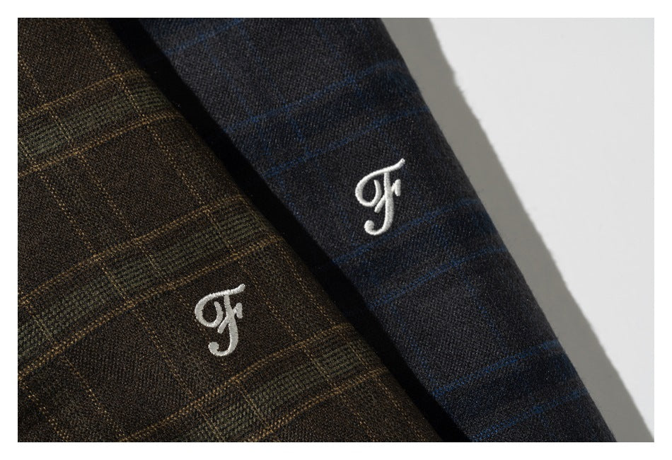 Close-up of white embroidered monograms on brown and navy plaid fabric.