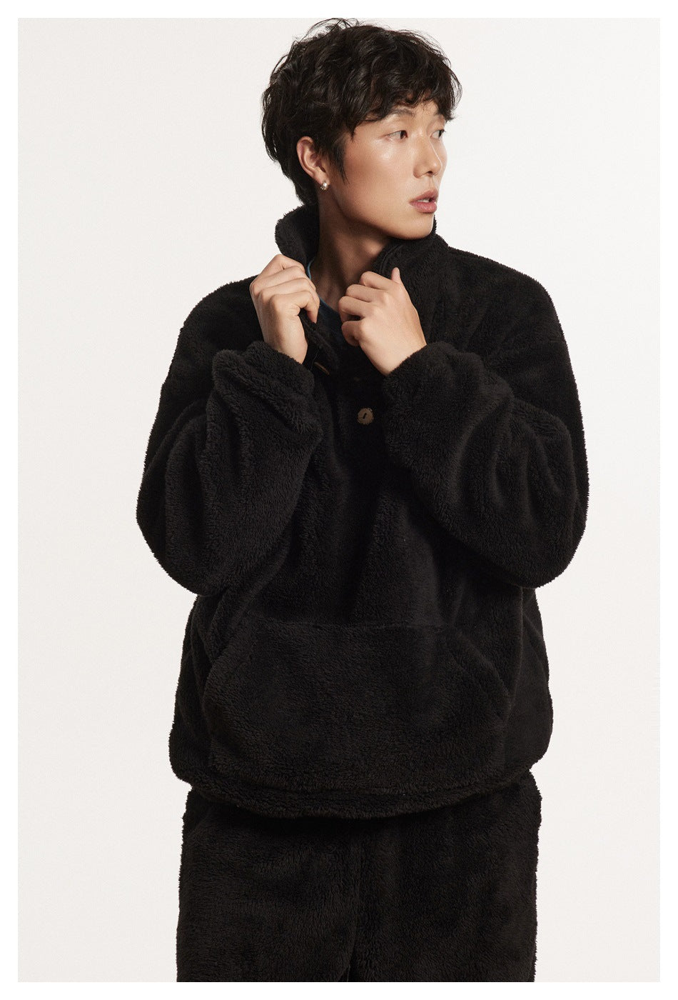 Model in a black plush collared pullover with buttons and a large front pouch pocket, paired with black pants.