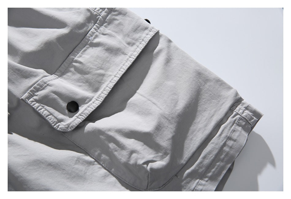 Close-up of a light gray cargo pocket with a black snap-fastened flap and stitched seams.