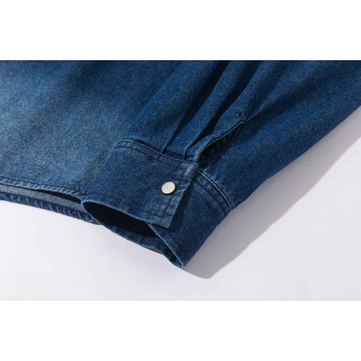 Close-up of a blue denim shirt sleeve cuff with a pale button.