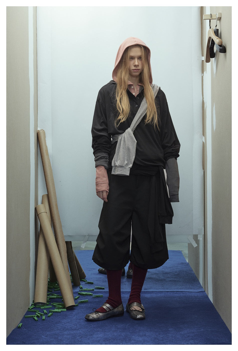 Model wearing a black layered outfit with a red-and-white striped hood and cuffs, wide cropped trousers, and a gray layer