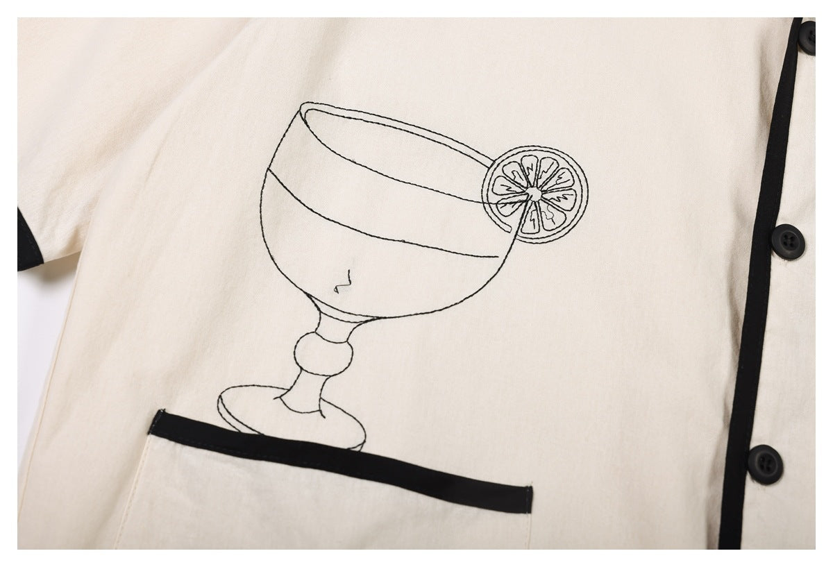 Cream garment detail with black piping, buttons, a pocket, and a line drawing of a citrus cocktail glass.