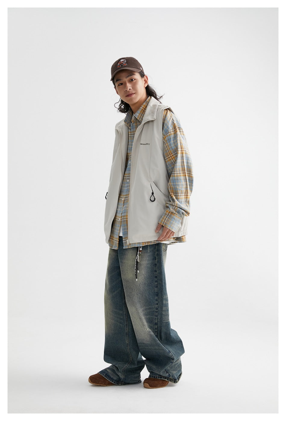 Full-length model wearing a light gray zip-front vest over a blue and tan plaid shirt with loose jeans.