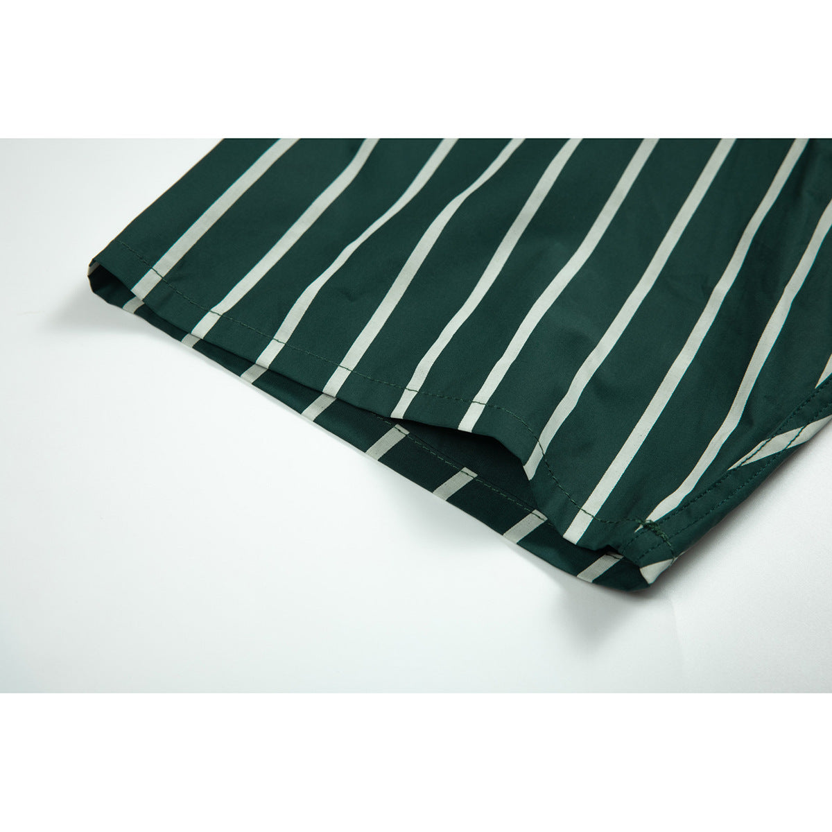 Close-up of the hem and stitching on a dark green shirt with thin cream stripes.