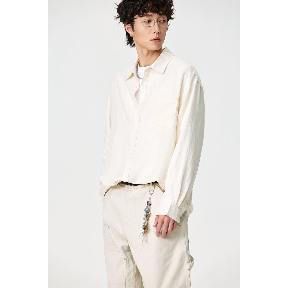 Model wearing an ivory button-up shirt with a pointed collar and chest pocket, paired with light trousers.