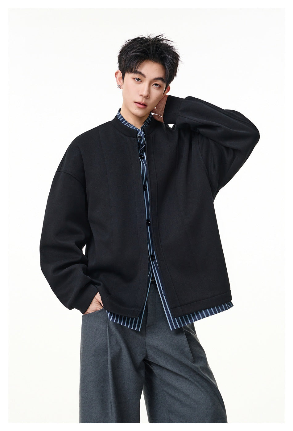 Model wearing a black oversized button-front jacket over a blue striped shirt, shown from the front.