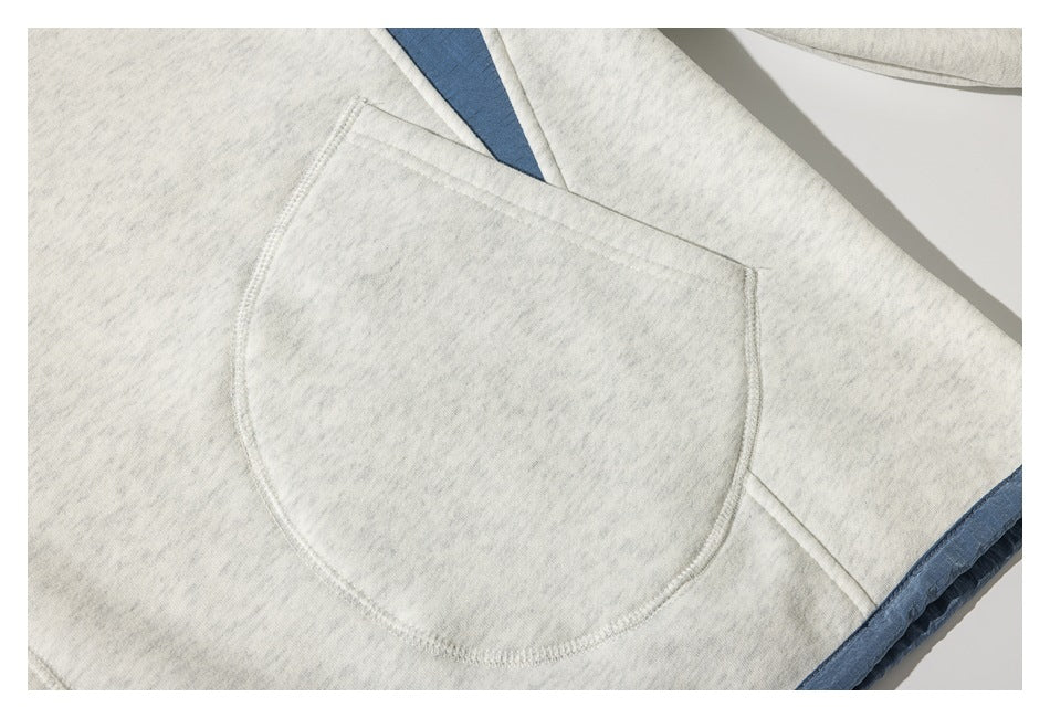 Close-up of a rounded pocket on a light heather-gray garment, with a blue accent visible beneath it.