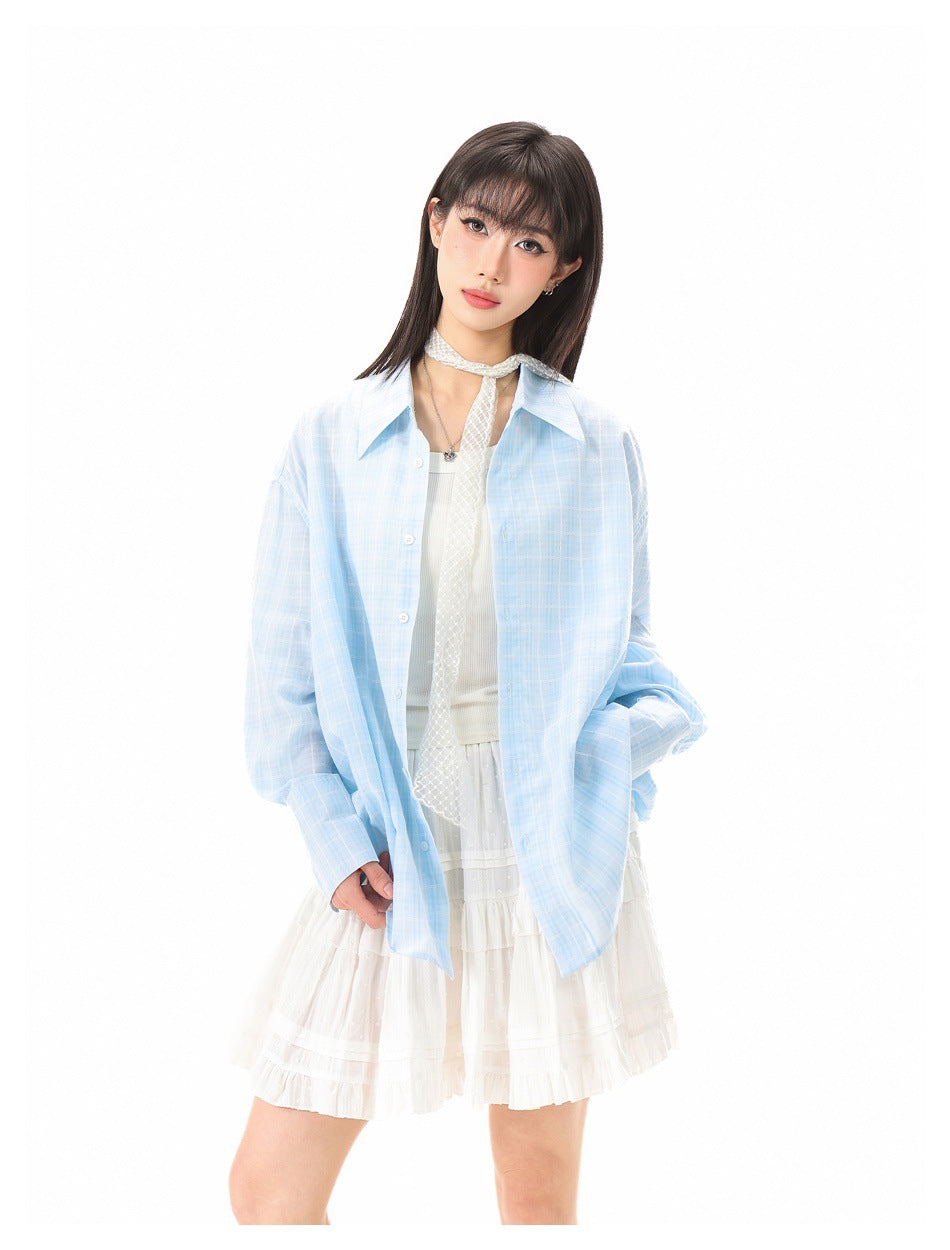 Model wearing an oversized light-blue plaid button-up shirt over a white outfit with a lace neck scarf.