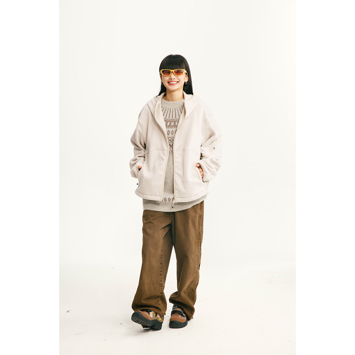 Model wearing an off-white hooded zip-up jacket over a knit sweater and brown trousers.