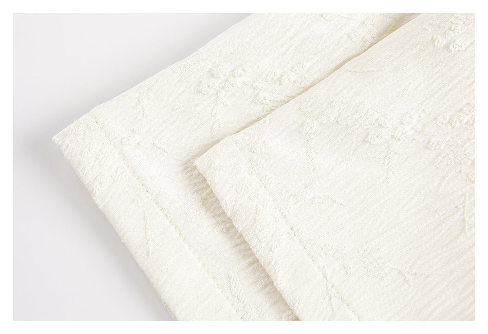 Close-up of overlapping cream garment edges with stitched hems and textured fabric.