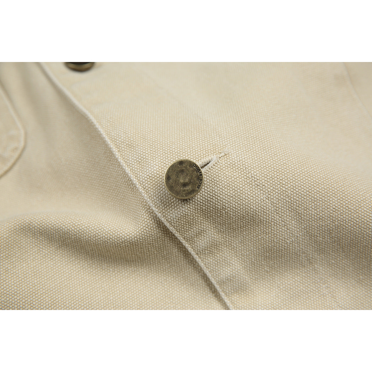 Close-up of a round metal jacket button on beige textured fabric.