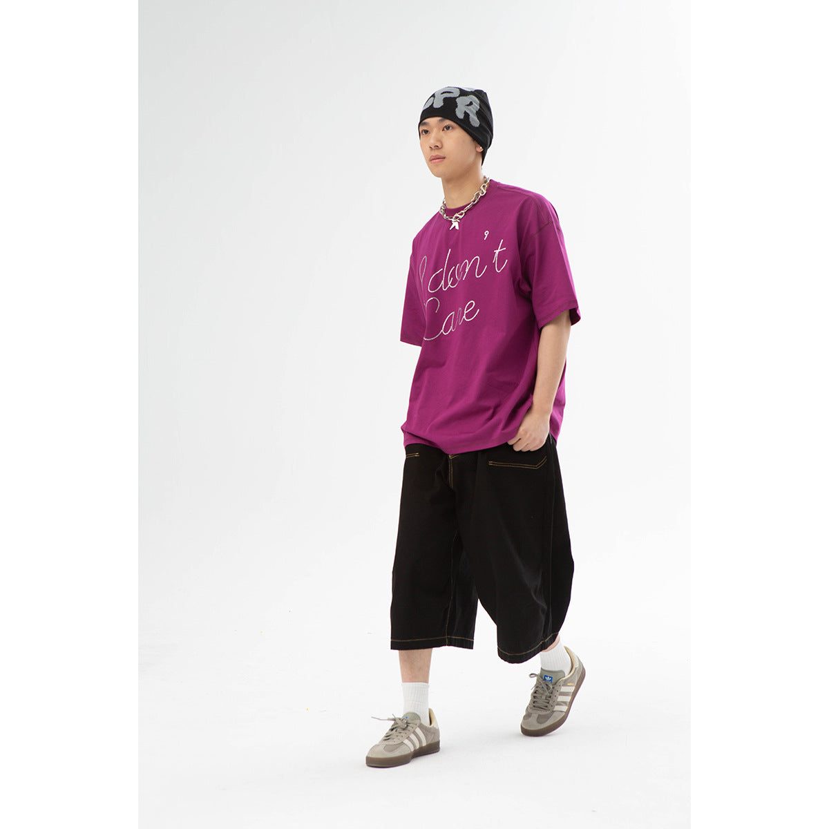 Model wearing a magenta oversized T-shirt with white cursive lettering and loose black shorts.