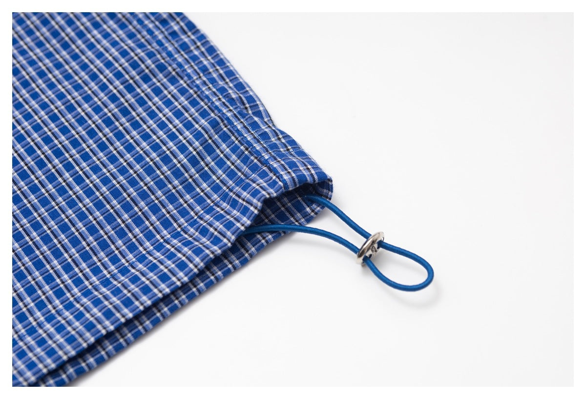 Blue plaid garment hem detail with an adjustable blue cord and metal toggle.