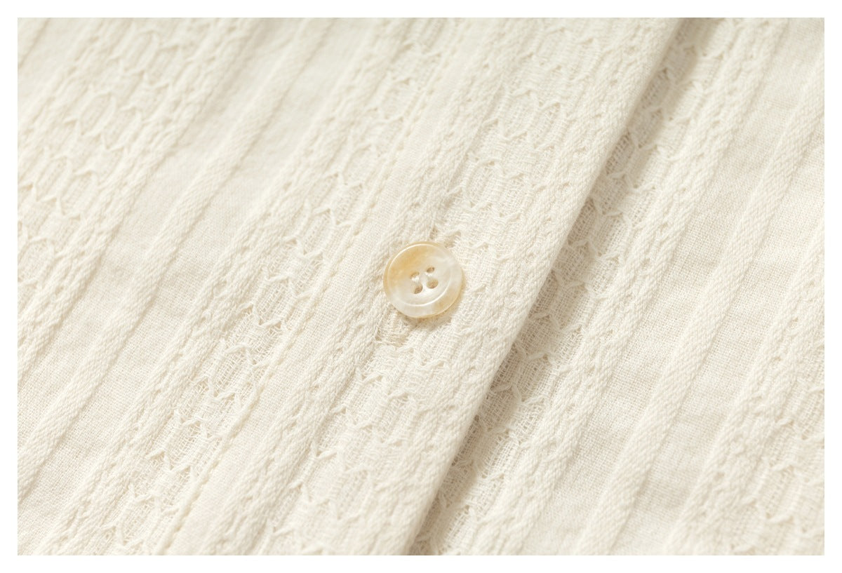 Close-up of a translucent cream four-hole button on textured ivory fabric with woven vertical patterns.