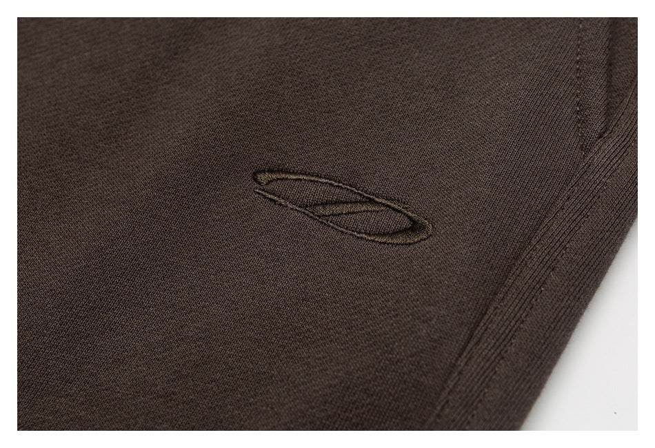 Close-up of a tonal embroidered oval logo on dark brown garment fabric.