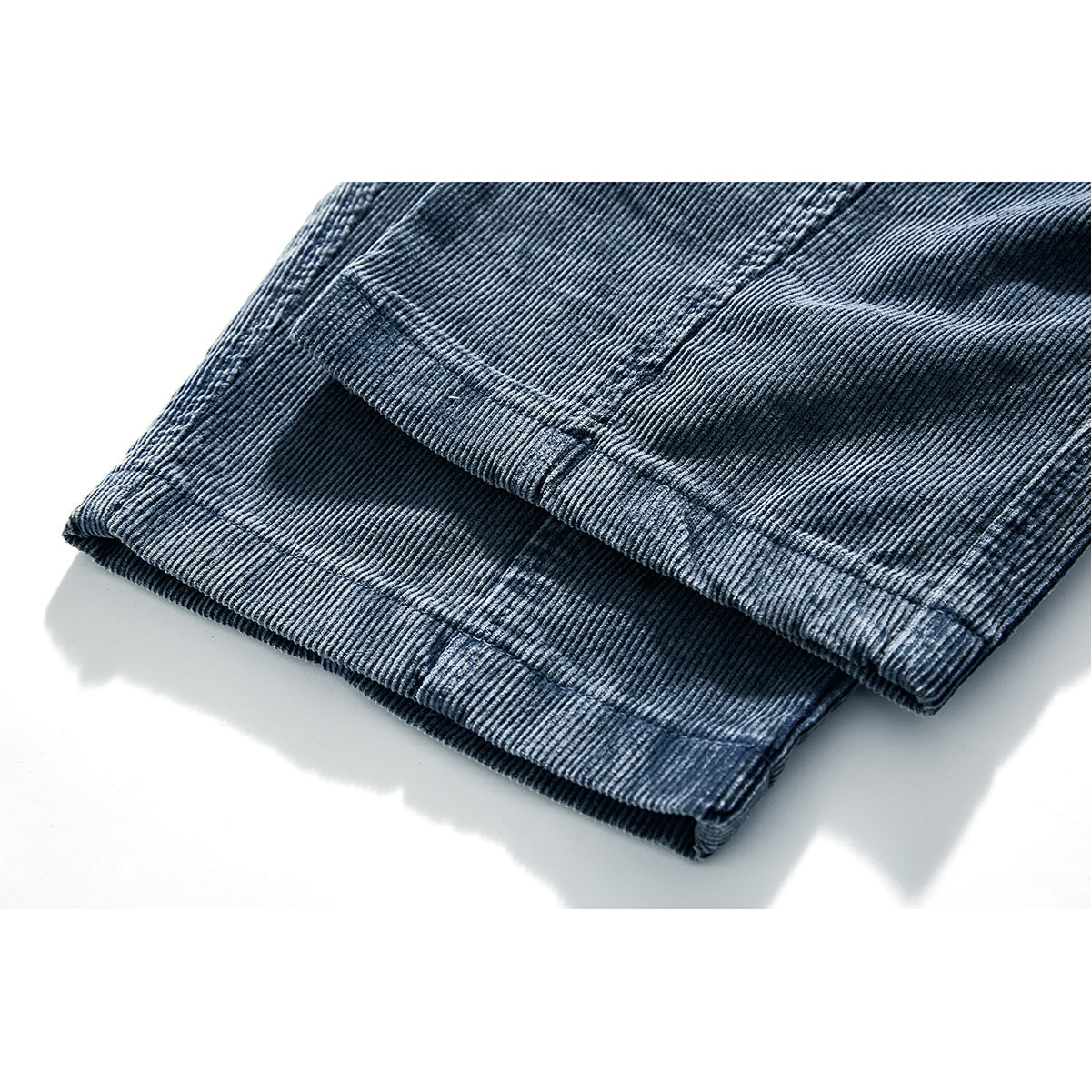Close-up of the folded hem of dark blue corduroy trousers, showing the ribbed texture and stitching.