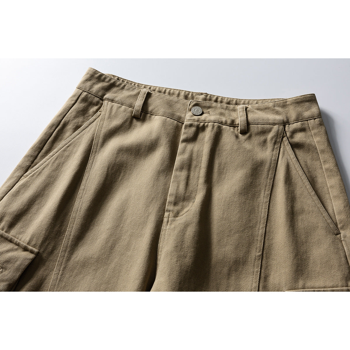 Close-up of the front waistband, button, belt loops and pleated front of khaki trousers.