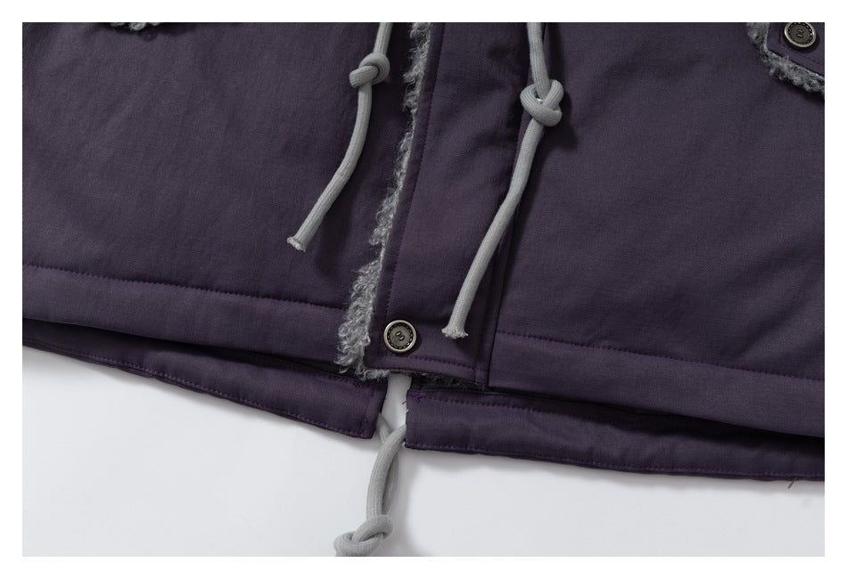 Close-up of a dark purple coat hem with gray knotted cords, a button, and fuzzy trim.