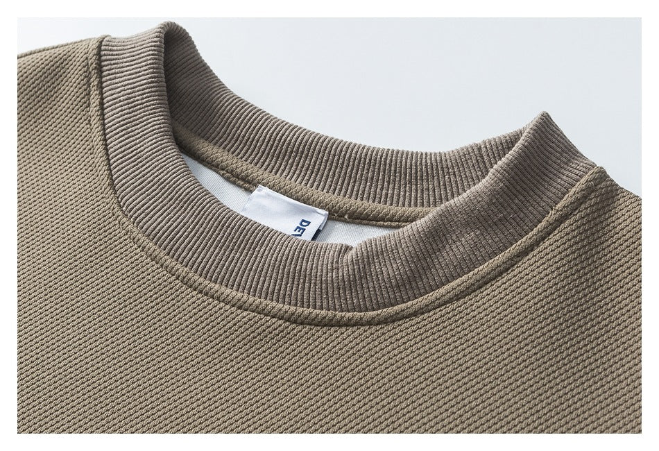 Close-up of the taupe sweatshirt’s ribbed crew neckline and textured fabric, with part of the inner label visible.