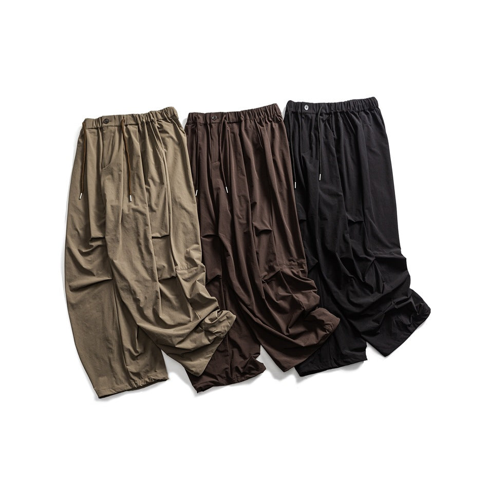 Three pairs of loose trousers in khaki, dark brown, and black, shown from the front with elastic waistbands and drawstrings.