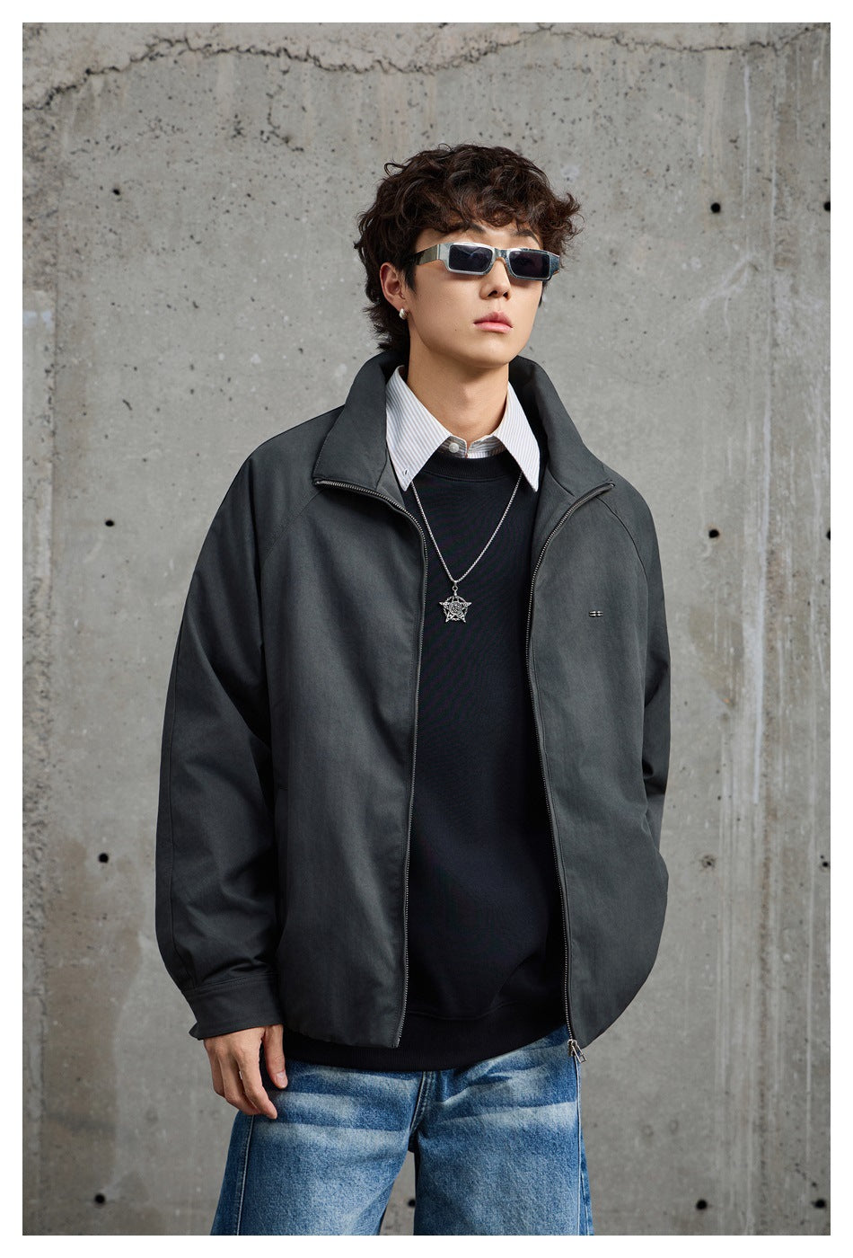 Model wearing an open charcoal-gray jacket over a black sweater and striped shirt, shown from the front.
