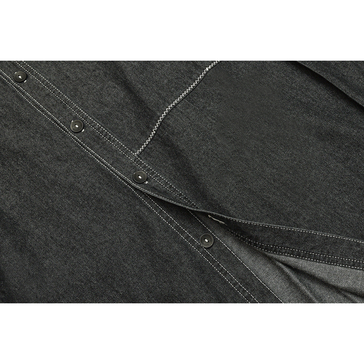 Close-up of a charcoal shirt placket with dark buttons, white topstitching, and a curved seam.