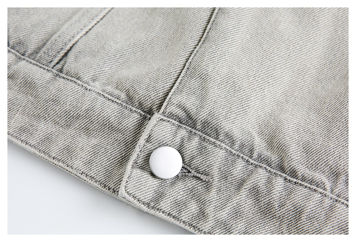 Close-up of a round silver button on the waistband of pale gray washed denim.