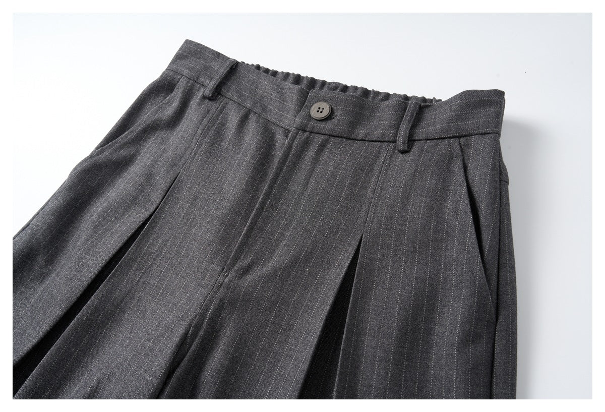 Angled close-up of dark charcoal pinstripe trousers showing the buttoned waistband, belt loops and front pleats.