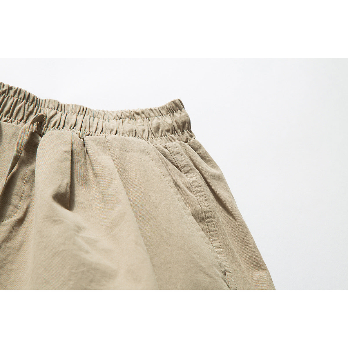 Close-up of tan shorts showing the elastic waistband, side pocket opening and stitching.