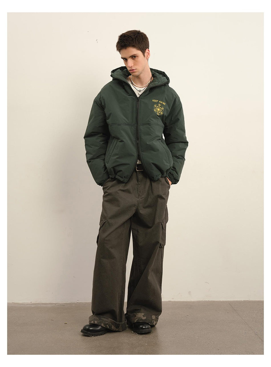 Full-length model wearing a dark green hooded jacket with yellow chest embroidery and loose dark cargo pants.