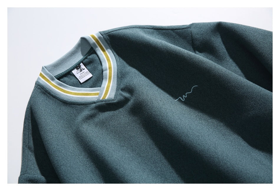 Close-up of a dark teal sweatshirt showing its striped V-neck trim and small embroidered chest mark.