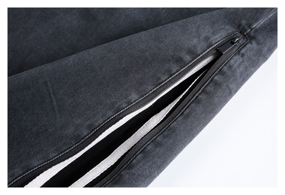Close-up of a partially open zipper along a dark charcoal jeans leg, revealing a light inner strip.