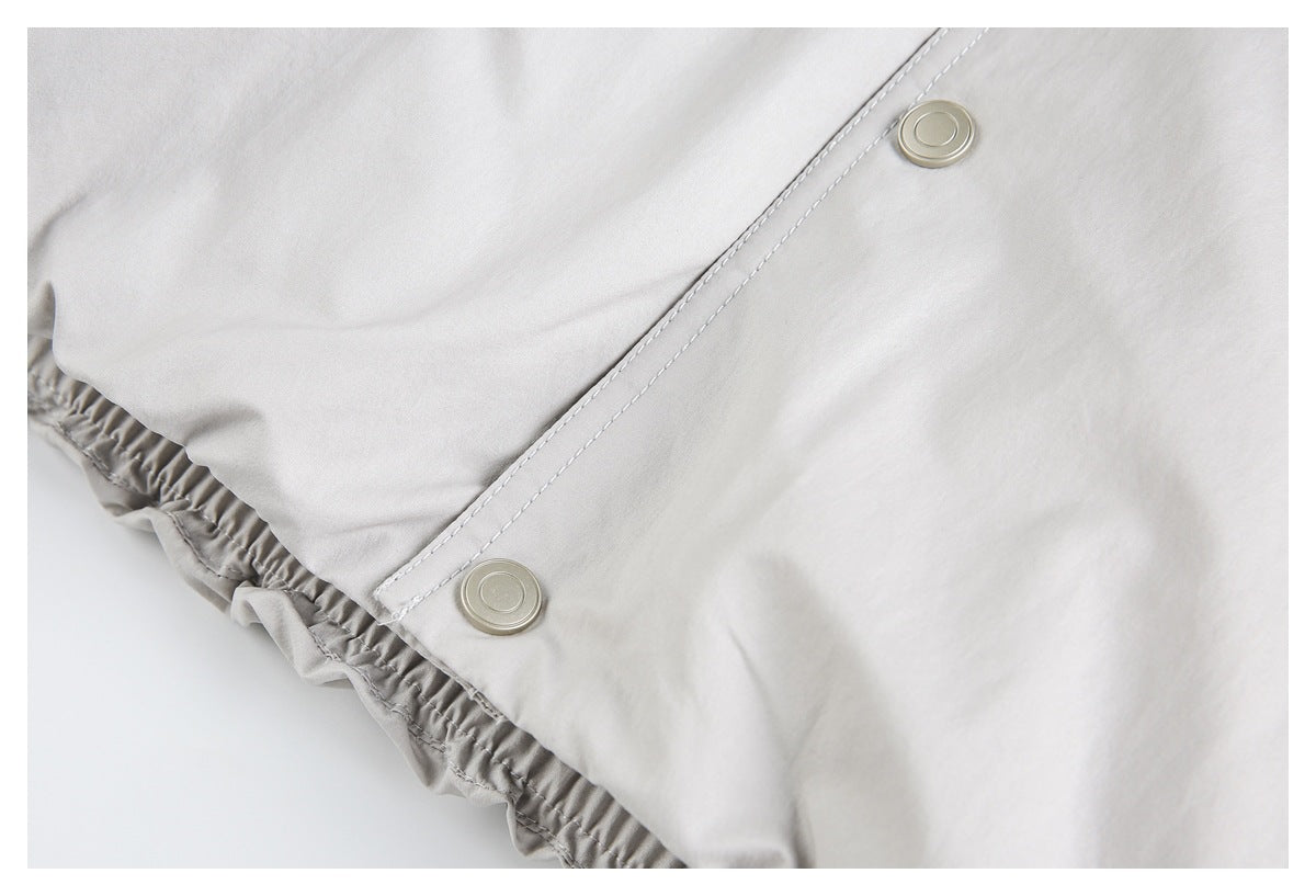 Pale gray garment detail showing two metal snaps along a stitched panel and a gathered elastic edge.