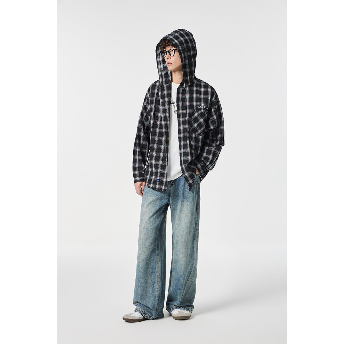 Full-length model wearing a black and gray plaid hooded button-up shirt, loose jeans, and sneakers.
