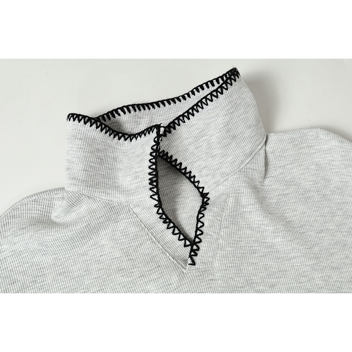 Close-up of a light gray ribbed top's collar with bold black blanket-stitch edging.
