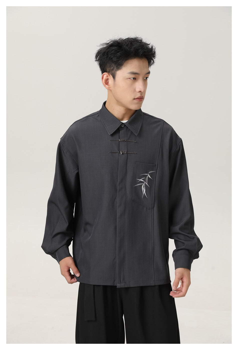 Model wearing a charcoal long-sleeve shirt with a pointed collar, twin metal fasteners, and embroidered bamboo on the chest