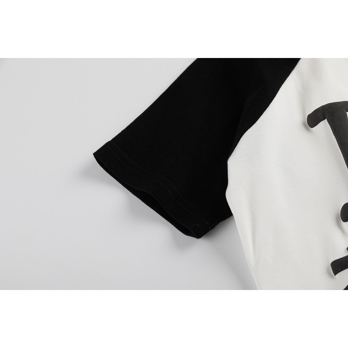 Close-up of the black sleeve and hem stitching on a white raglan shirt.