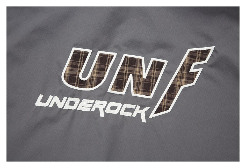 Close-up of a garment logo reading “UNF UNDEROCK” in white and brown plaid lettering on dark gray fabric.