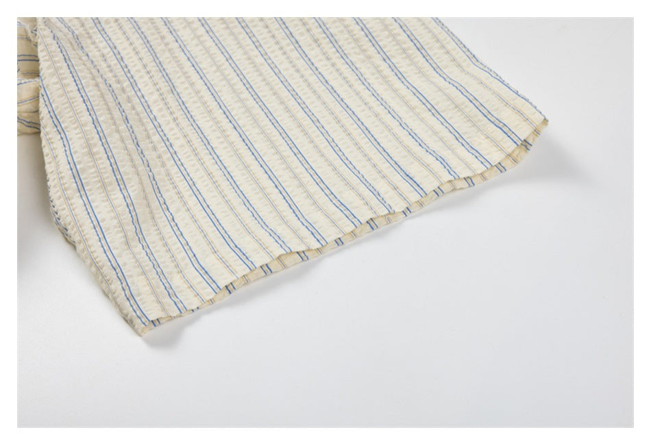 Close-up of a cream garment hem with narrow blue vertical stripes and stitched edging.